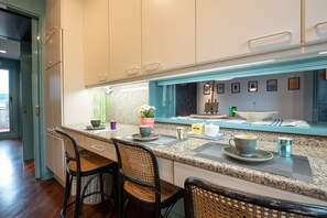 A modern kitchen with white cabinets, a granite countertop, and a breakfast bar with wicker chairs. - Tiffany's Apartment Flaminio (Roma)
