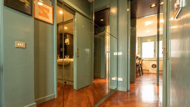A hallway with a wooden floor, mirrored walls, and a view into a bathroom with a sink and toilet. - Tiffany's Apartment Flaminio (Roma)
