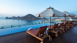 A deck with lounge chairs and umbrellas overlooking a clear blue sea and distant mountains. - Corazon Cabo - Beachfront 2 bed/2 bath Suite with HOT TUB! (Cabo San Lucas)