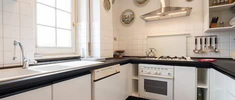 Een keuken met witte kastjes, een zwart aanrecht, een raam, een fornuis en decoratieve borden aan de muur.