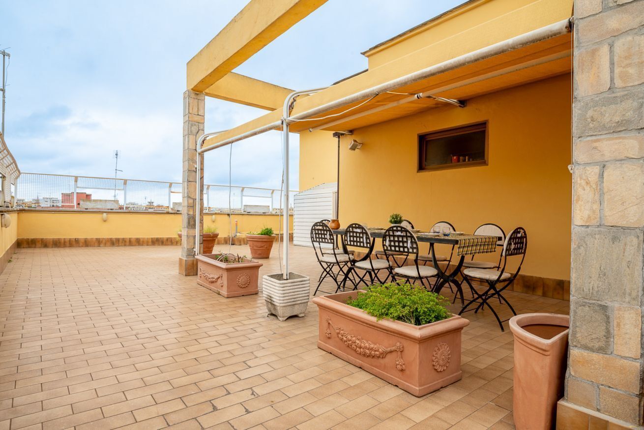 A rooftop terrace with a table and chairs, potted plants, and a view of the cityscape.