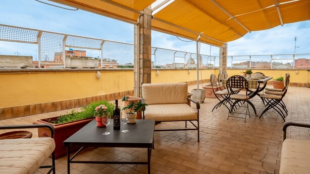 A rooftop terrace with outdoor seating, a table, and potted plants. - La Terrazza di Paola San Giovanni (Roma)