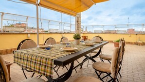 A rooftop terrace with a checkered tablecloth, chairs, a table set for dining, and a yellow canopy. - La Terrazza di Paola San Giovanni (Roma)