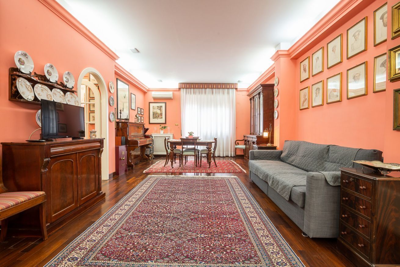 Een woonkamer met een bank, een televisie, een houten kast, een eettafel met stoelen en een kamerkleed met een patroon.