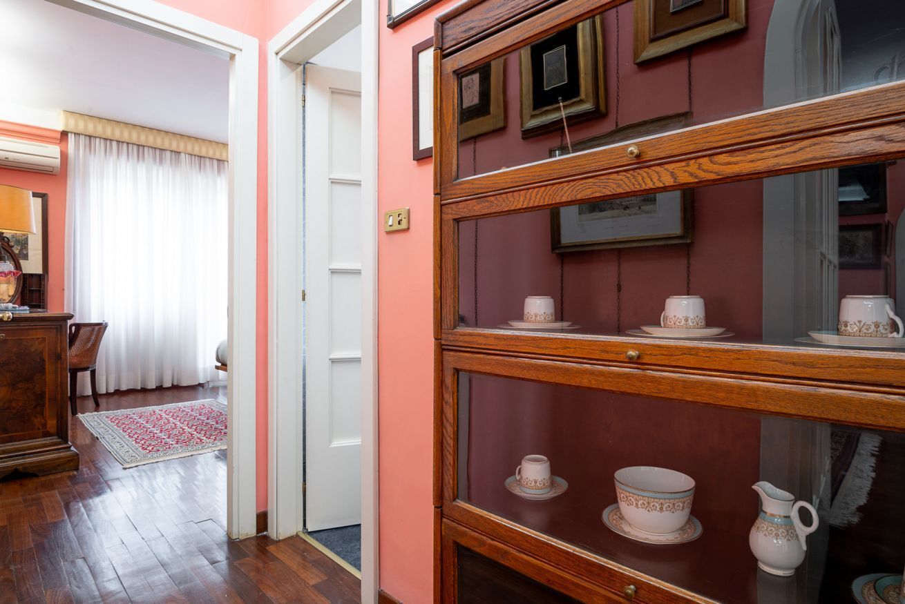 Een kamer met een houten kast waarin theeserviezen staan, een houten vloer, een witte deur en een rode muur.