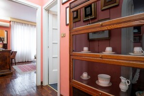 A room with a wooden cabinet displaying tea sets, a wooden floor, a white door, and a red wall. - La Terrazza di Paola San Giovanni (Roma)