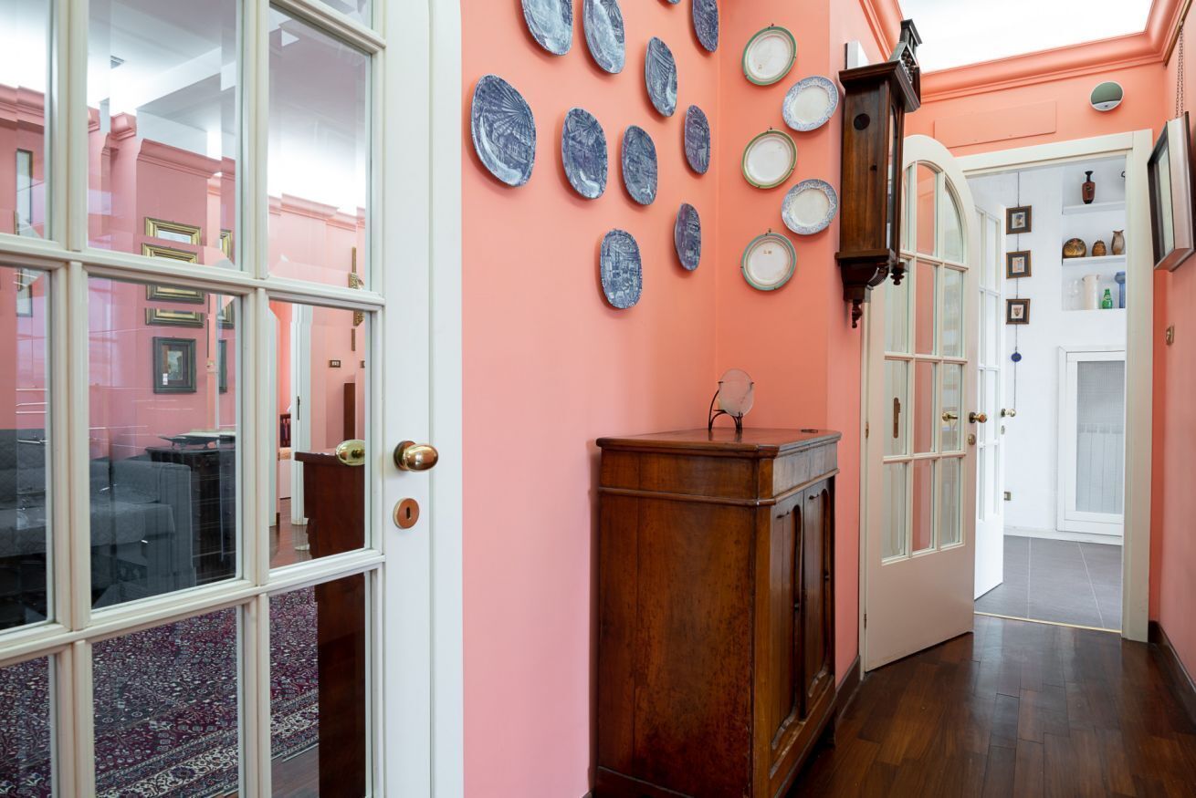 A hallway with a pink wall, a wooden cabinet, and a door leading to another room.
