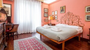 A bedroom with a wooden bed, a desk with a chair, a large window with curtains, and a patterned rug. - La Terrazza di Paola San Giovanni (Roma)