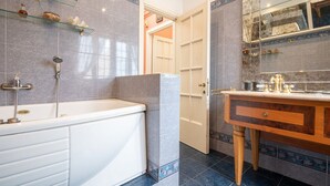 A bathroom with a bathtub, a vanity with a mirror, and shelves with toiletries. - La Terrazza di Paola San Giovanni (Roma)