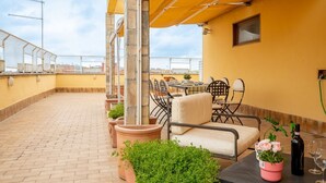 A rooftop patio with a table and chairs, potted plants, and a yellow awning. - La Terrazza di Paola San Giovanni (Roma)