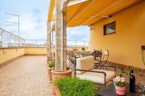 Eine Dachterrasse mit Tisch und Stühlen, Topfpflanzen und einem gelben Markisenvorbau.