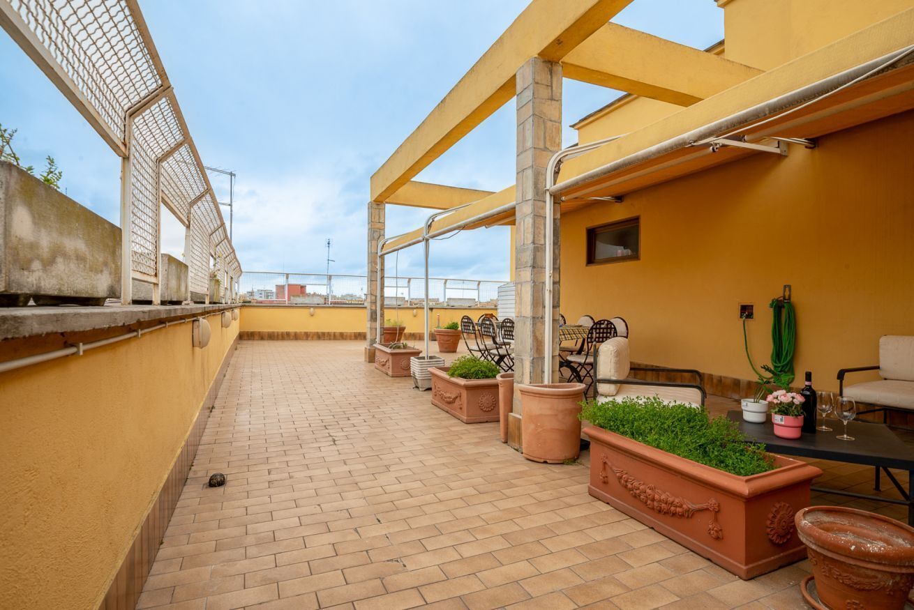 A rooftop terrace with brick flooring, outdoor seating, potted plants, and a yellow wall.