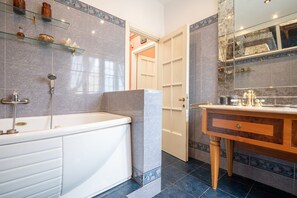 Ein Badezimmer mit einer Badewanne, einem Waschtisch inklusive Spiegel und Ablagen für Toilettenartikel.