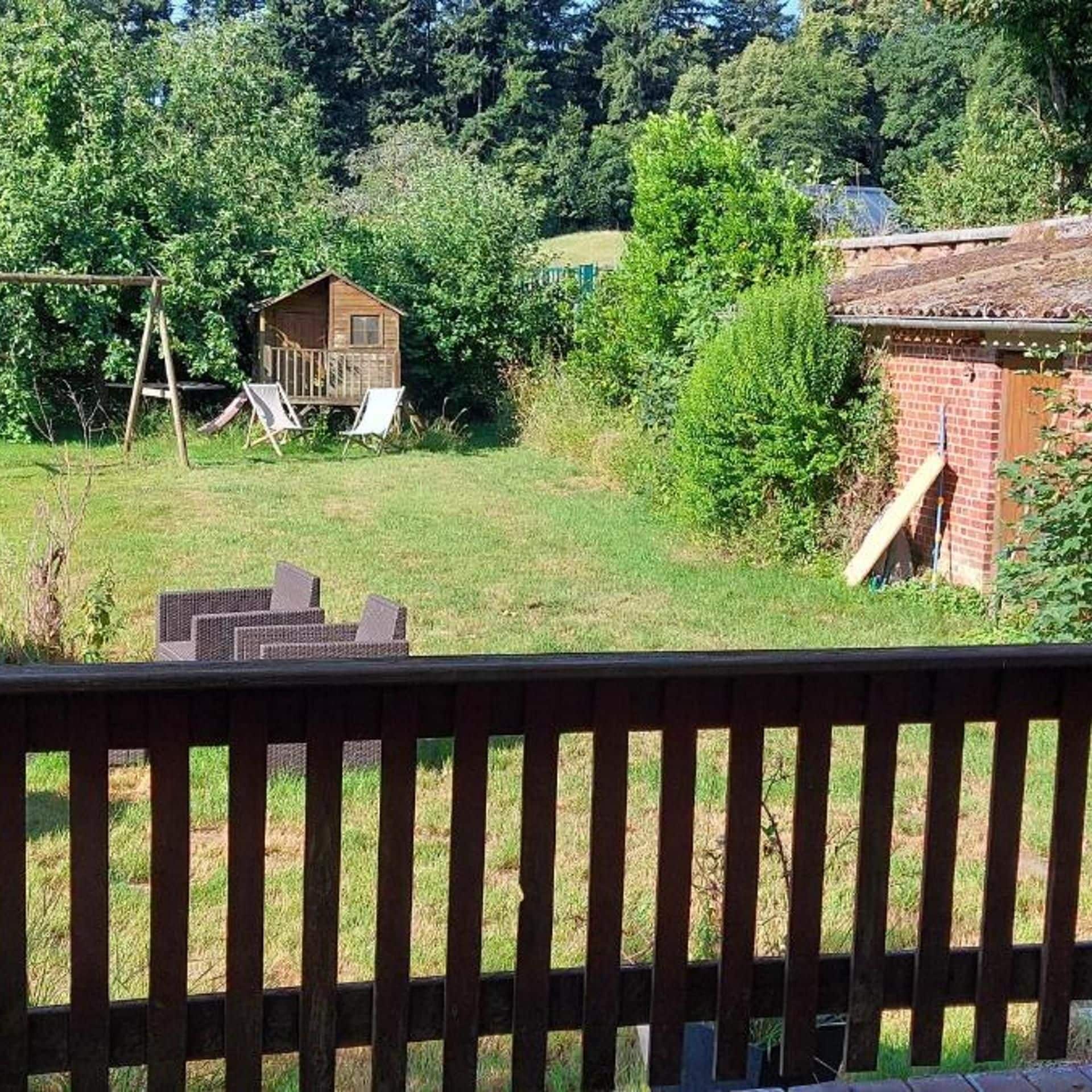 A backyard with a wooden playhouse, a brick building, and a swing set.