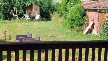 A backyard with a wooden playhouse, a brick building, and a swing set.