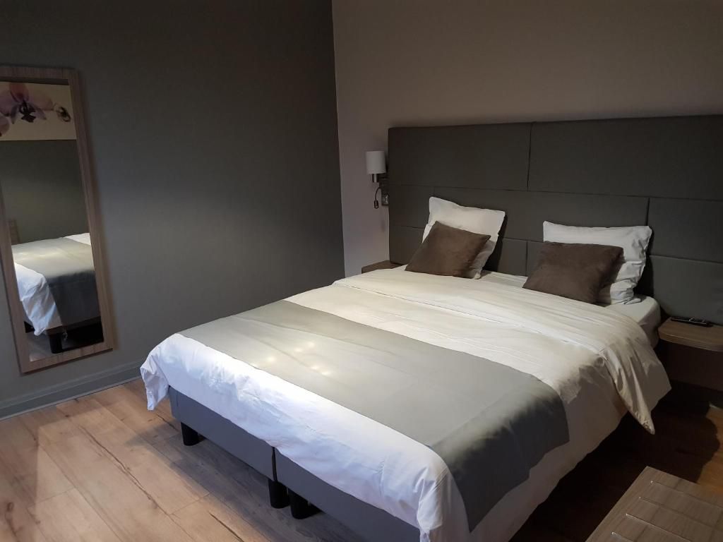 Een netjes opgemaakt bed met een hoofdeinde, een bedlampje en een spiegel aan de muur.