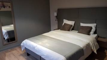 Een netjes opgemaakt bed met een hoofdeinde, een bedlampje en een spiegel aan de muur.