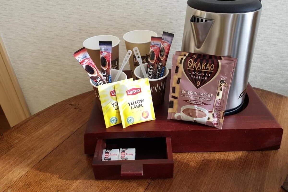 A coffee station with a coffee maker, cups, Lipton tea bags, and Okakao chocolate powder.
