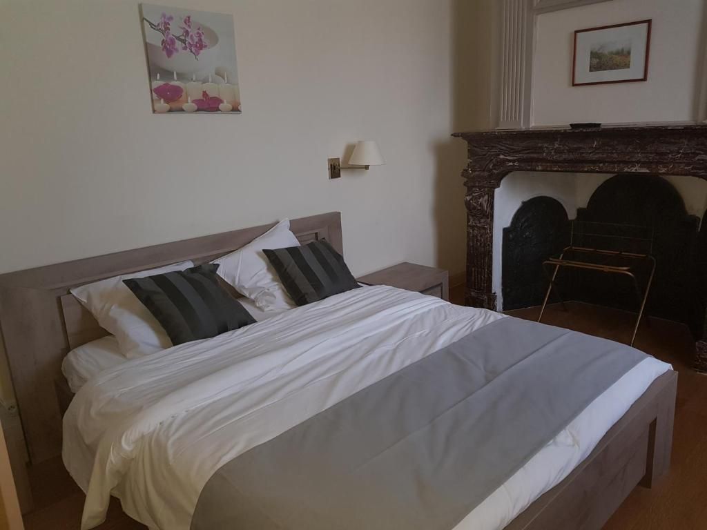 Un letto rifatto con una testiera, un comodino e una lampada. È presente un caminetto con mensola e un quadro incorniciato sopra.