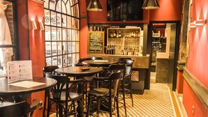 Zona de bar con mesas y sillas redondas, un tablero de menú y una barra repleta de botellas.