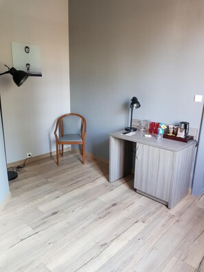 Ein kleiner, moderner Raum mit einem Holzbstuhl, einem Schreibtisch mit Lampe und einer kleinen Küchenzeile.