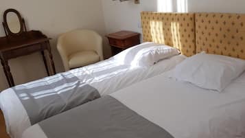 A hotel room with a double bed, a small bedside table, a chair, a desk with a mirror, and a wall-mounted lamp.