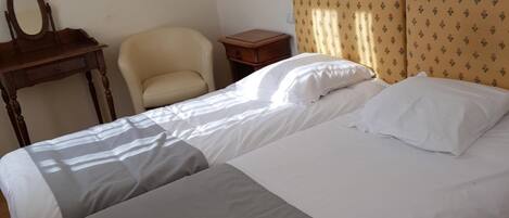 Una habitación de hotel con una cama doble, una mesita de noche pequeña, una silla, un escritorio con un espejo y una lámpara de pared.