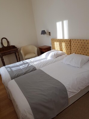 Ein Hotelzimmer mit einem Doppelbett, einem kleinen Nachttisch, einem Sessel, einem Schreibtisch mit Spiegel und einer Wandlampe.