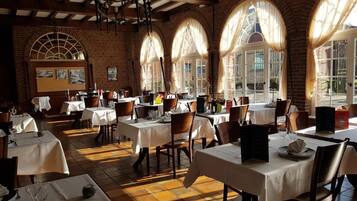 A restaurant with multiple tables and chairs, brick walls, and large windows with curtains.