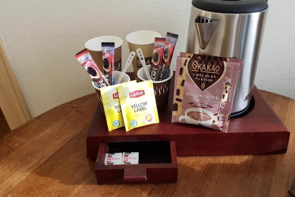 Una estación de café con cafetera, tazas, bolsitas de té Lipton y cacao en polvo Okakao.