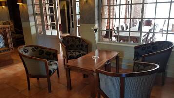 A dining area with a wooden table and four chairs, a vase on the table, and a view through a window.
