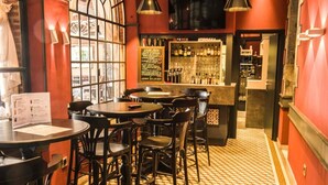 Zona de bar con mesas y sillas redondas, un tablero de menú y una barra repleta de botellas.