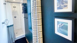 A bathroom with a shower, a towel rack, and a curtain. There are framed pictures on the wall. - The Little Black House - in the heart of RiNo! (Denver)