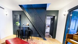 A modern living room with a staircase, a red leather ottoman, and a piano. - The Little Black House - in the heart of RiNo! (Denver)