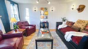 A living room with a sofa, armchair, coffee table, and a bookshelf. - The Little Black House - in the heart of RiNo! (Denver)