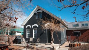 A two-story house with a black exterior and white trim, a front porch with a bench, and a small tree in the yard. - The Little Black House - in the heart of RiNo! (Denver)
