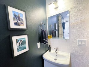 A bathroom with a white sink, a mirror, and two framed pictures on the wall. - The Little Black House - in the heart of RiNo! (Denver)