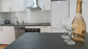 Eine moderne Küche mit weißen Schränken, einer Edelstahl-Dunstabzugshaube, einem Geschirrspüler und einer Weinflasche mit Gläsern auf der Arbeitsplatte.