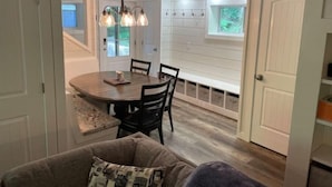 A dining area with a round table, chairs, and pendant lighting. There is a window with a view of greenery outside. - Blue Ridge Riverfront Cabin•2-Level Deck•Sleeps 8 (Blue Ridge)