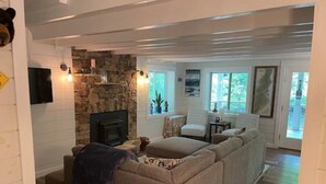 A cozy living room with a stone fireplace, a large beige sectional sofa, and a small round table with chairs. - Blue Ridge Riverfront Cabin•2-Level Deck•Sleeps 8 (Blue Ridge)