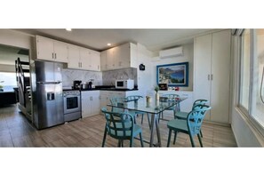 A modern kitchen with stainless steel appliances, white cabinets, and a glass dining table with teal chairs. - Penthouse with ocean and lagoon views (Cancún)