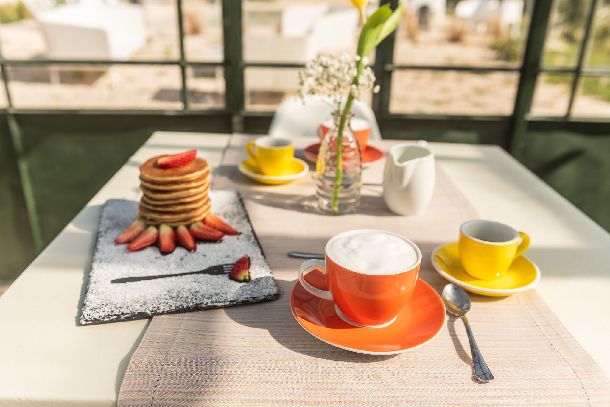 Une table dressée pour le petit-déjeuner, avec des crêpes, des fraises et du café.