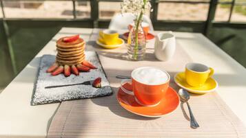 Une table dressée pour le petit-déjeuner, avec des crêpes, des fraises et du café.