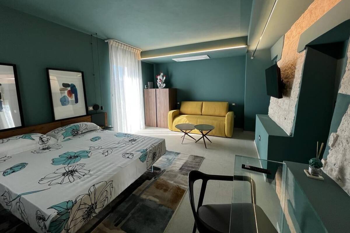 Et moderne hotelværelse med en seng, en gul lænestol, et lille bord og et glas skrivebord.