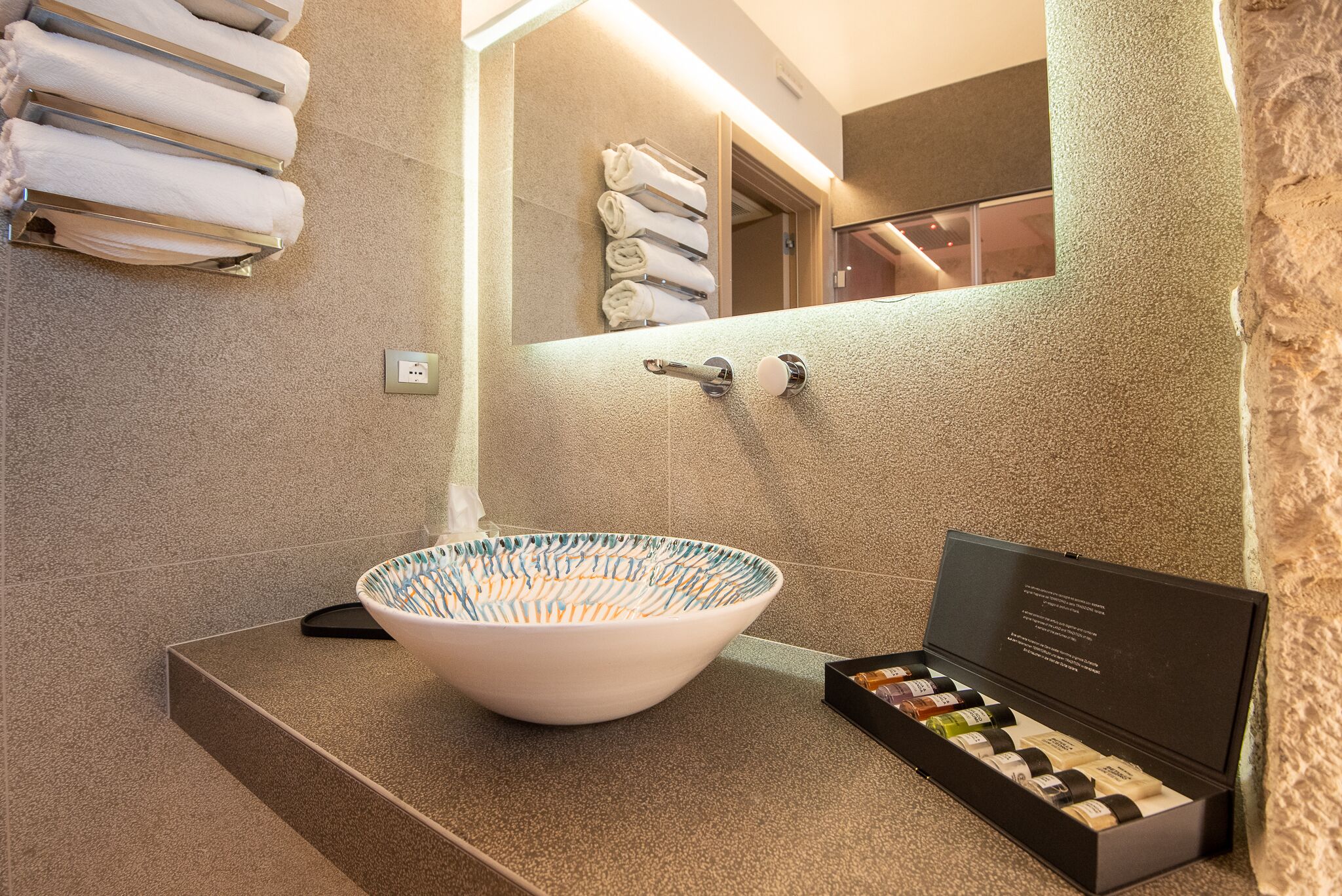 Une salle de bain avec un grand lavabo en forme de cuvette, un porte-serviettes et une boîte contenant des articles de toilette.