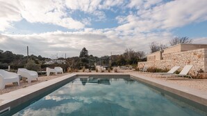 A swimming pool with white lounge chairs and a stone wall. - Villa Ada trulli in Puglia (Martina Franca)
