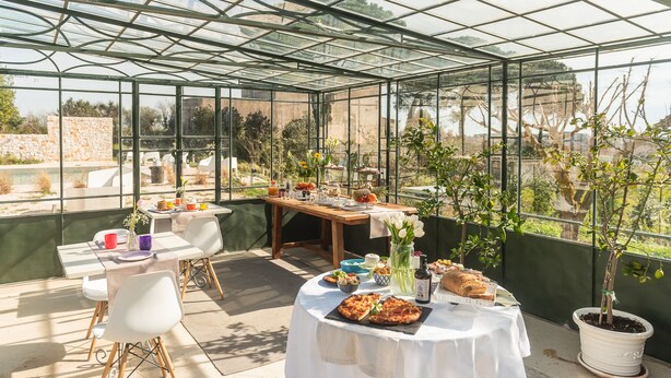 A greenhouse with tables set for a meal, surrounded by potted plants and flowers. - Villa Ada trulli in Puglia (Martina Franca)