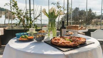 Una mesa con pizza, ensalada, pan y un jarrón de tulipanes en una terraza con vistas.