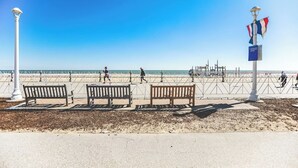 Una platja amb tres bancs de fusta, un fanal blanc i un pal amb banderes.
