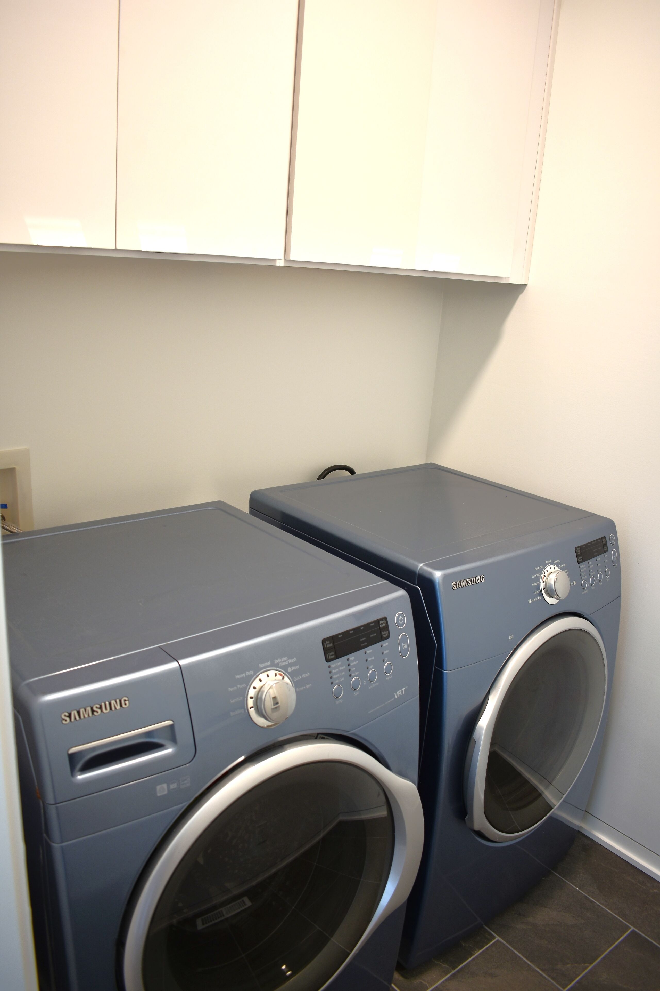 Two Samsung front-loading washing machines in a laundry room with white cabinets above.